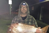 A man wearing a hoodie jumper and holding a fish.