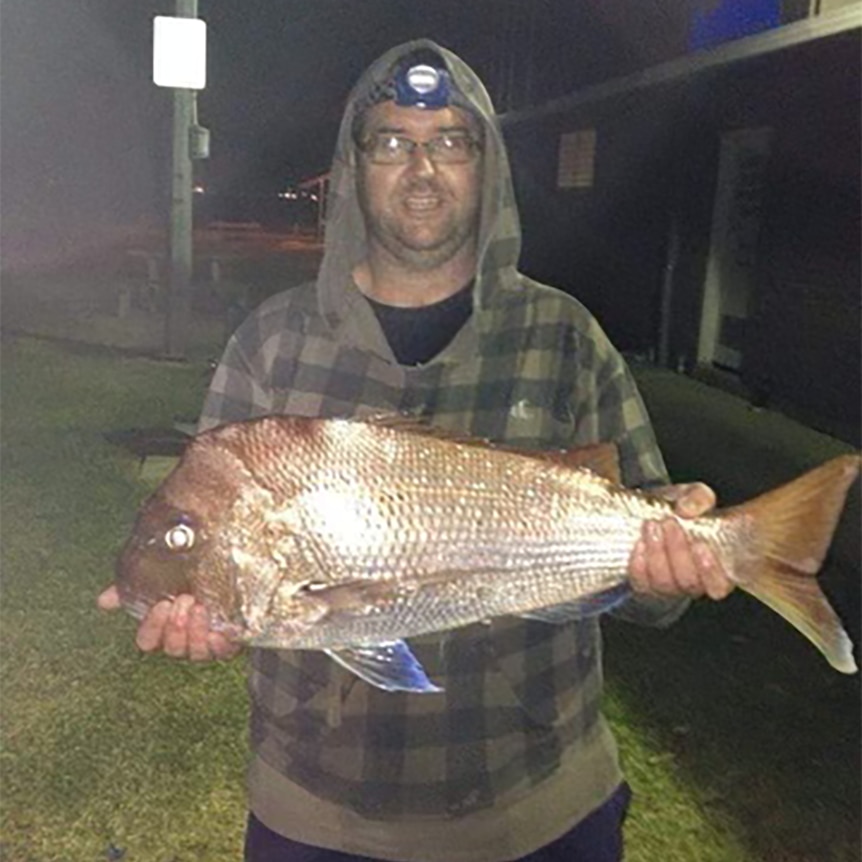 A man wearing a hoodie jumper and holding a fish.