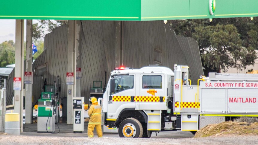 A Country Fire Service officer standing next to his truck looks at the collapsed underside of the awning over the fuel pumps.