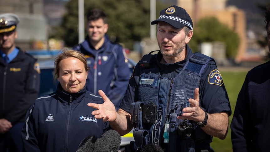 A police officer in uniform gestures while speaking to media.