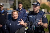 A police officer in uniform gestures while speaking to media.