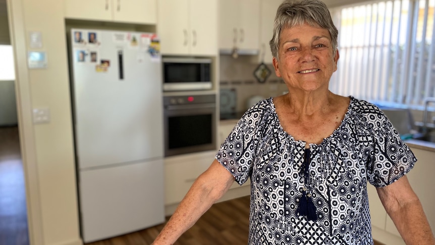 A woman smiles in her small kitchen. she wears a black and white patterned top with a tassel at the front