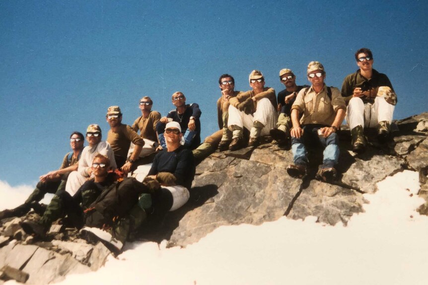 Historic photo of a group of men in sunglasses sitting on a rocky outcrop.
