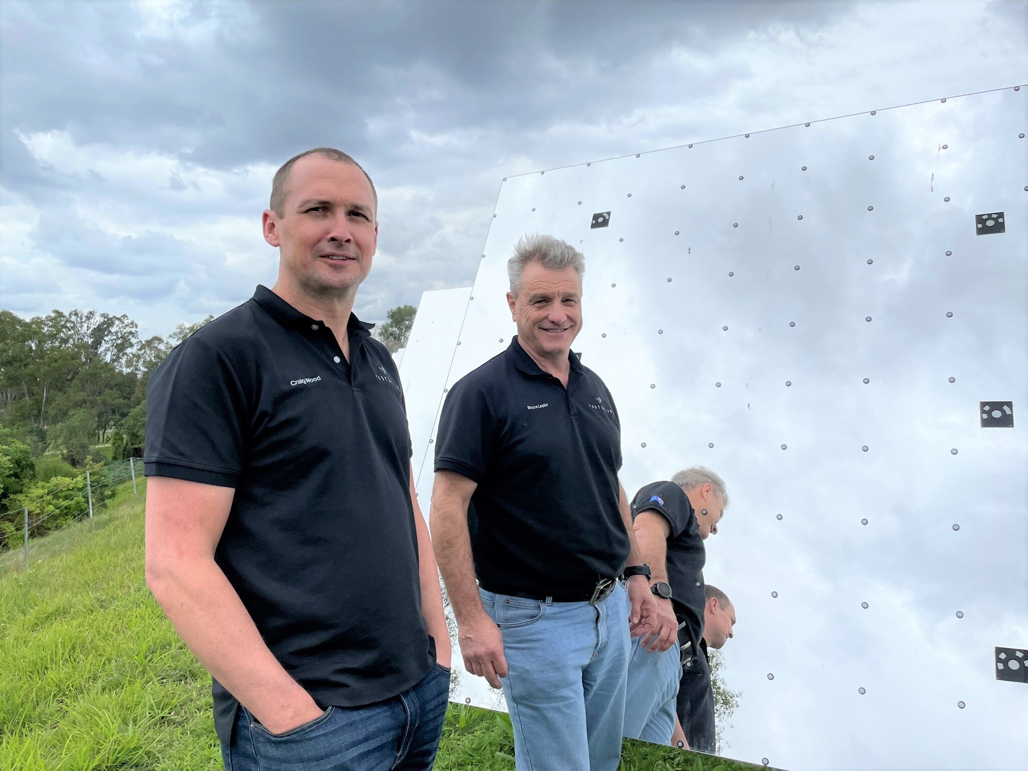Two men stand next to a giant mirror in a paddock