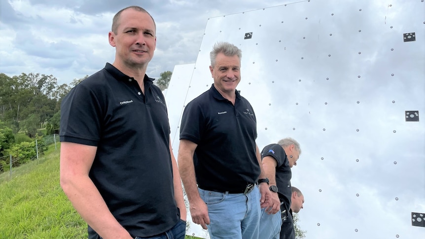 Two men stand next to a giant mirror in a paddock