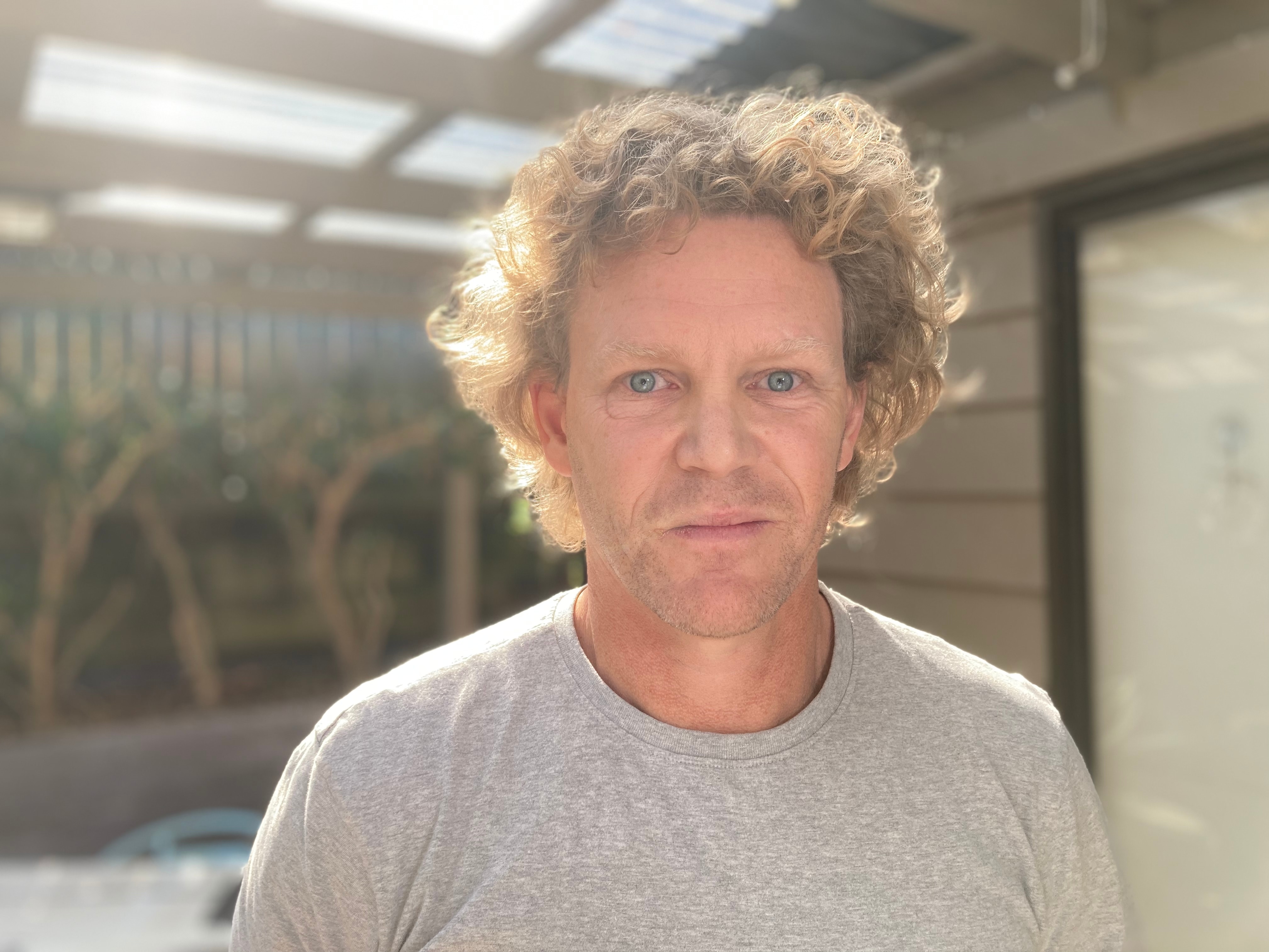 Man in gray t-shirt, curly blond hair, unsmiling