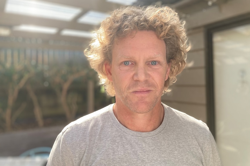 Man in gray t-shirt, curly blond hair, unsmiling