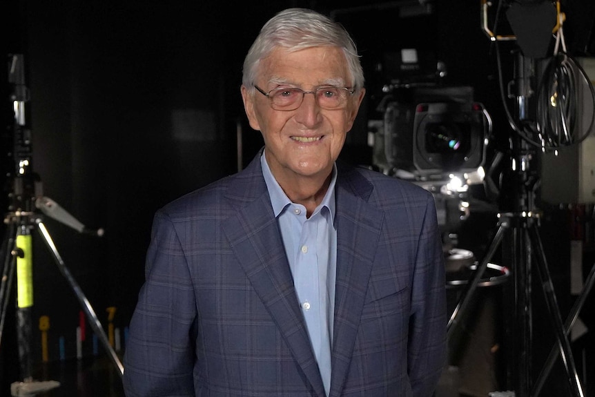 Michael Parkinson stands next to a TV camera.