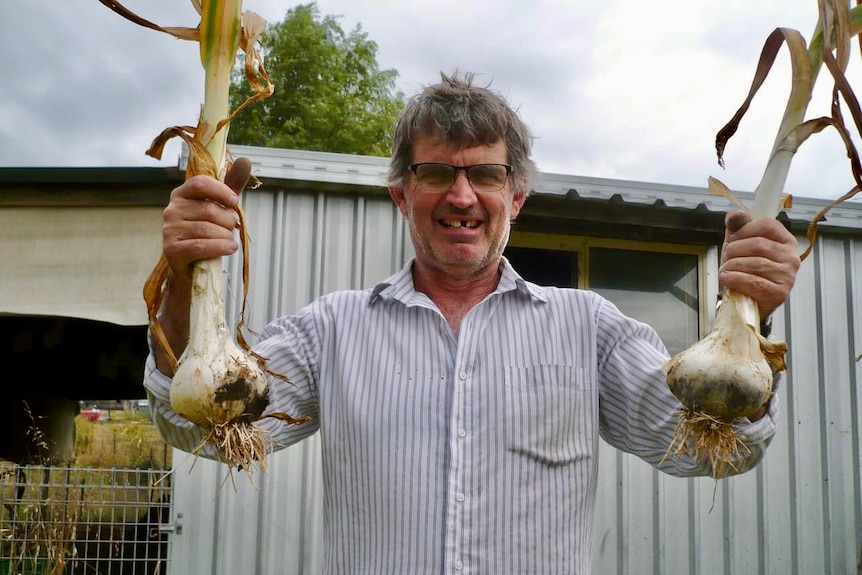 A man holds up two giant garlic chives and smiles.