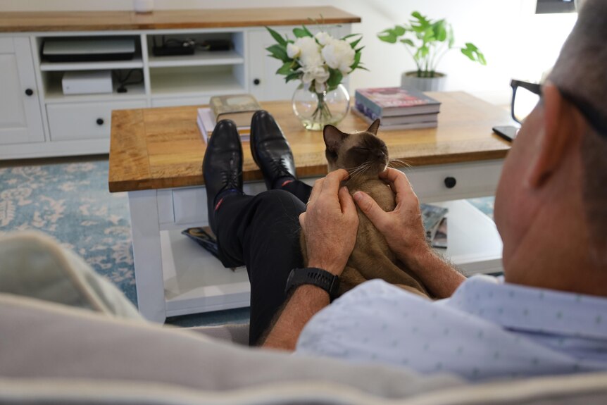 Dr Paul Nylander holds his cat Coco, while sitting on a couch.
