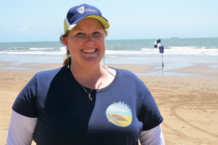 A white woman in her 30s with blonde hair,  smiling, wearing a navy cap and shirt. 