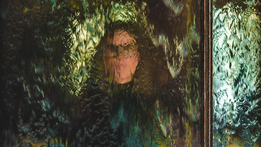 A person can be seen through a wall of water, reflecting blue and green light