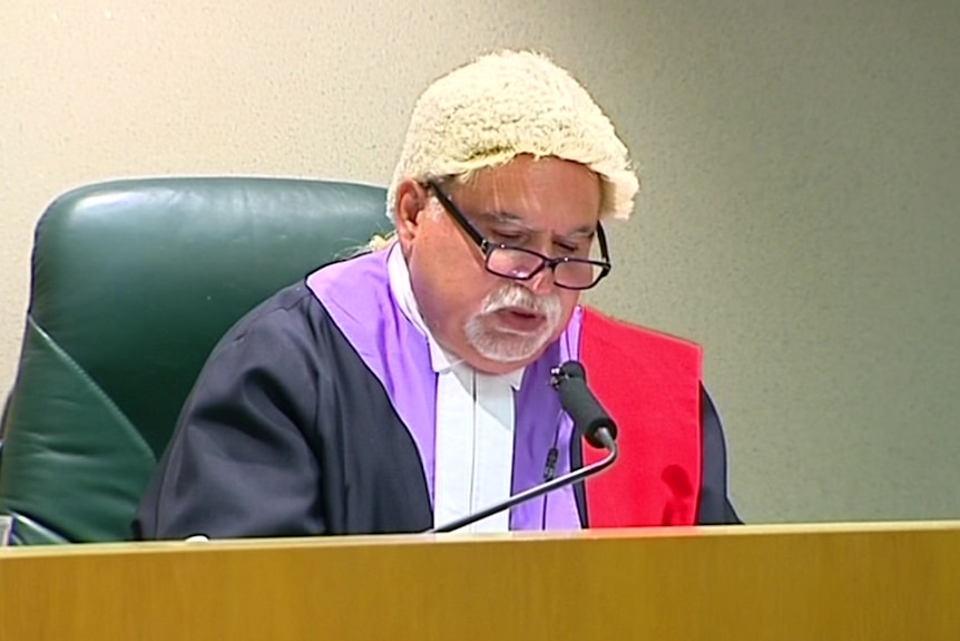 a man wearing a wig and sitting behind a desk