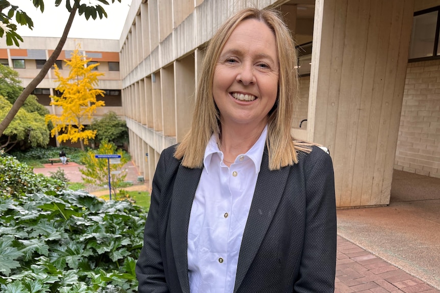 A white woman with blonde hair standing in a university campus courtyard