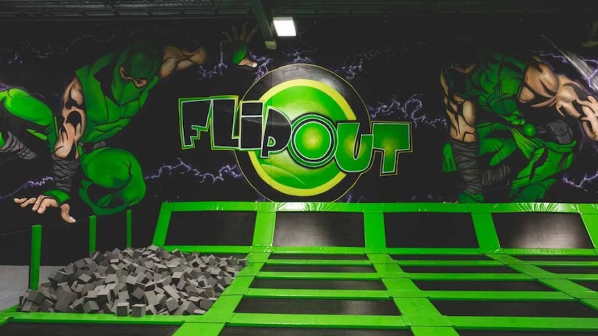 Green trampolines with a mural reading "FLIP OUT" behind.