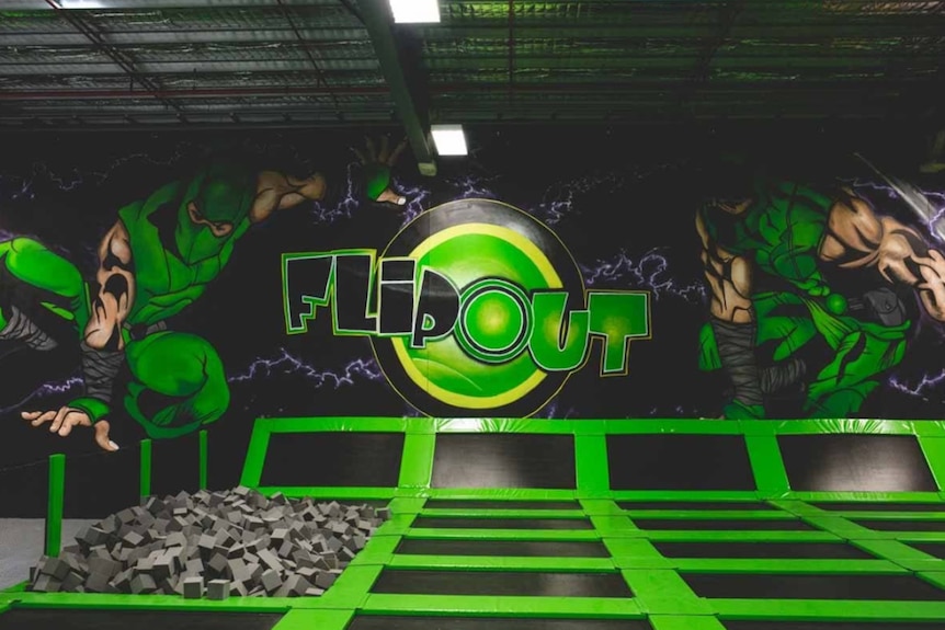 Green trampolines with a mural reading "FLIP OUT" behind.