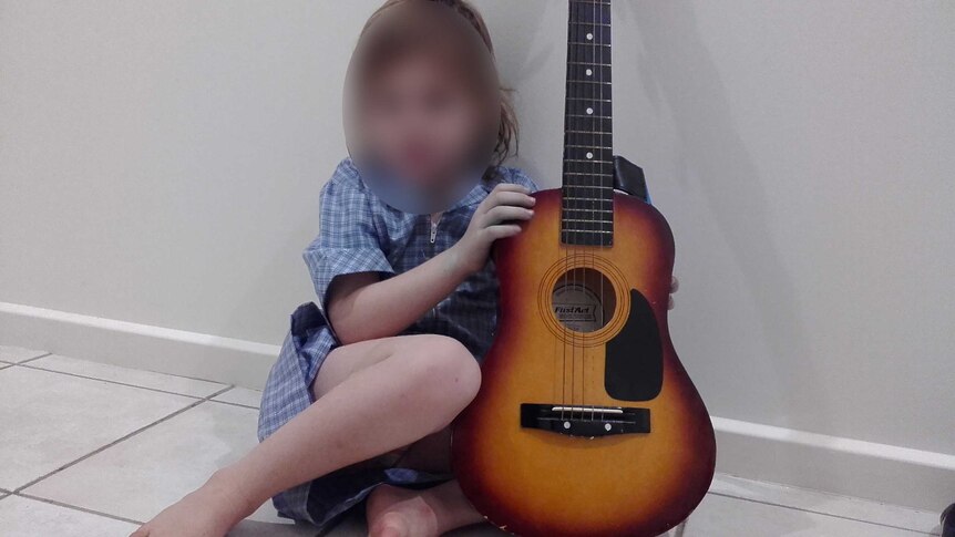 A child sits next to a guitar