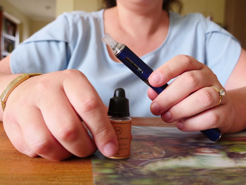 A close up of a woman holding a vape and a bottle of vape liquid