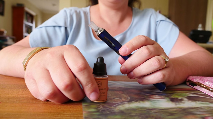 A close up of a woman holding a vape and a bottle of vape liquid