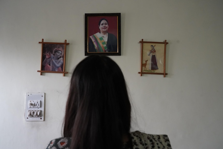 The back of a woman's head as she looks at a wall with her mother's portrait on it. 