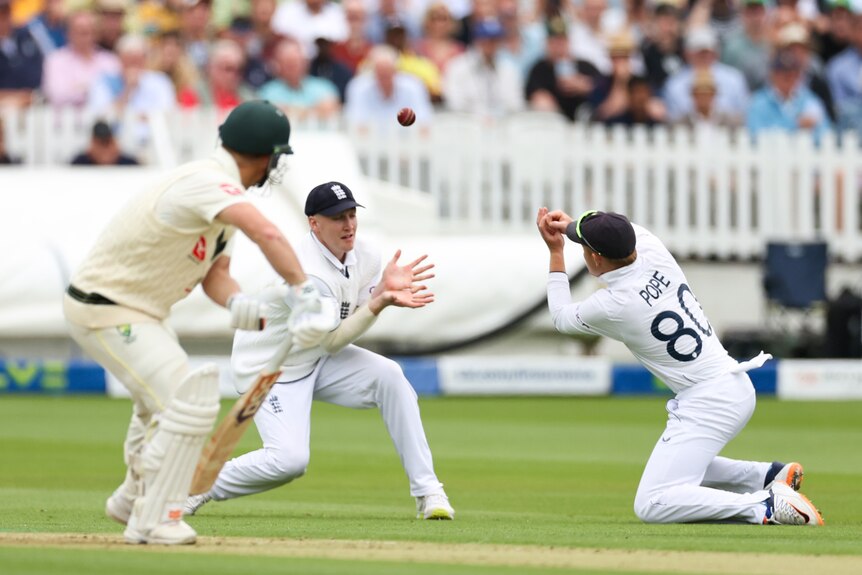 A cricket ball flies away from England fielder Ollie Pope as Australia batter David Warner watches on.