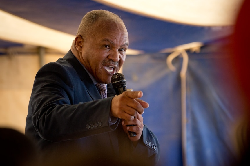 Jonas de Koker points towards his congregants while delivering a sermon iunder a marquee.