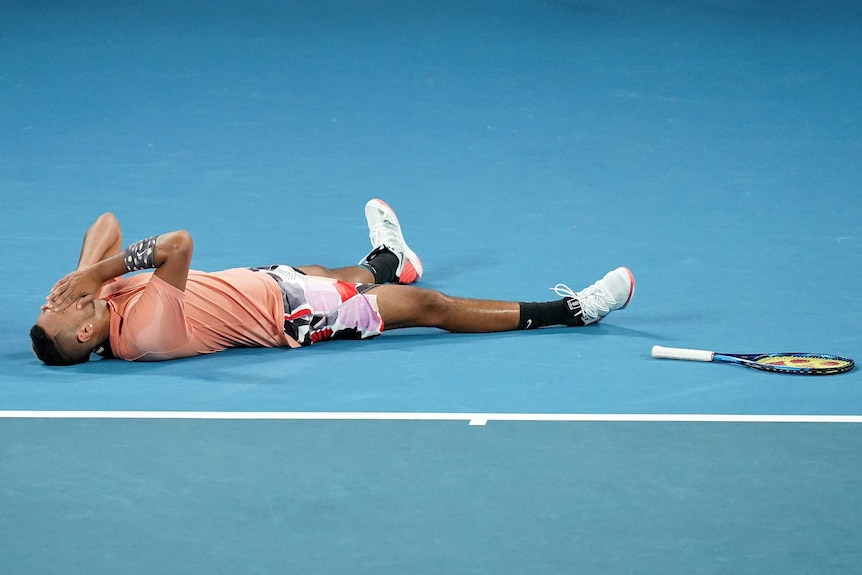 A male tennis player lies on a court with his hands on his face after winning a match at the Australian Open.