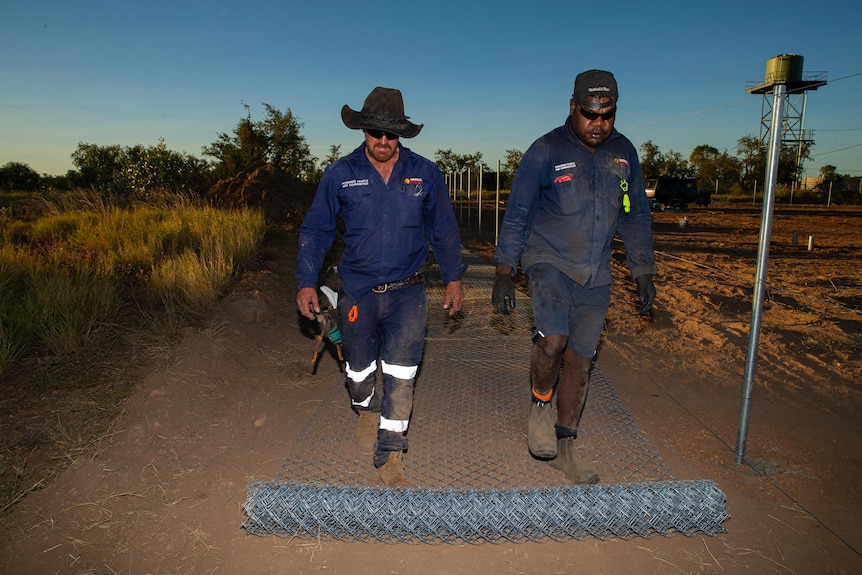 A photo showing two tradies rolling out wire on the ground with water tank on ground.