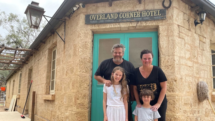 A family of four stands in front of a blue door and a sign