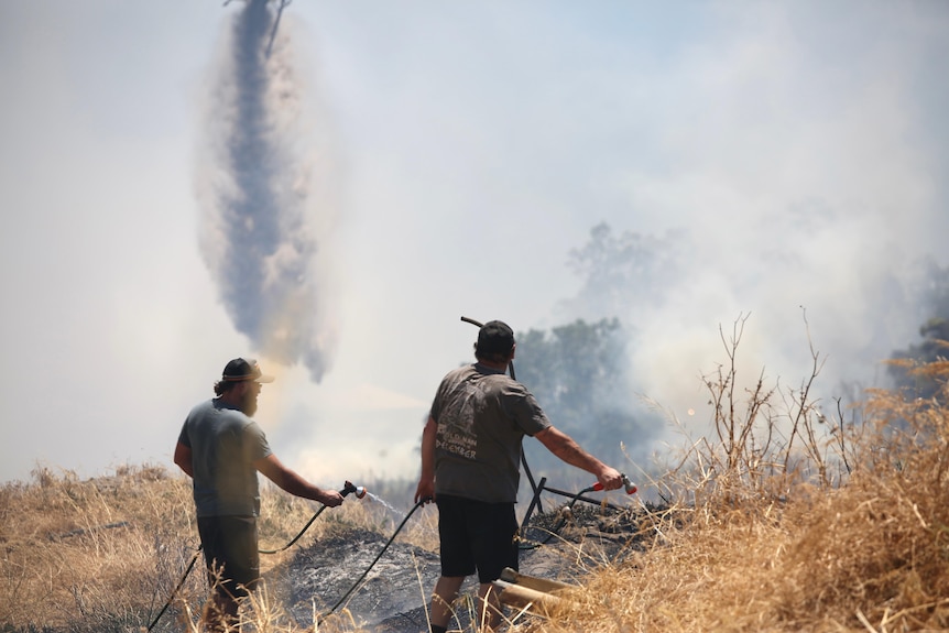 Residents fight a scrub fire in Aubin Grove as a plane drops water from the air.