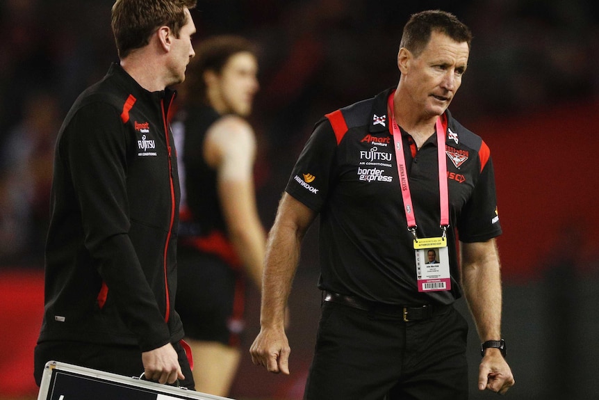 An AFL coach looks dejected as his assistant holding a magnet board looks on.