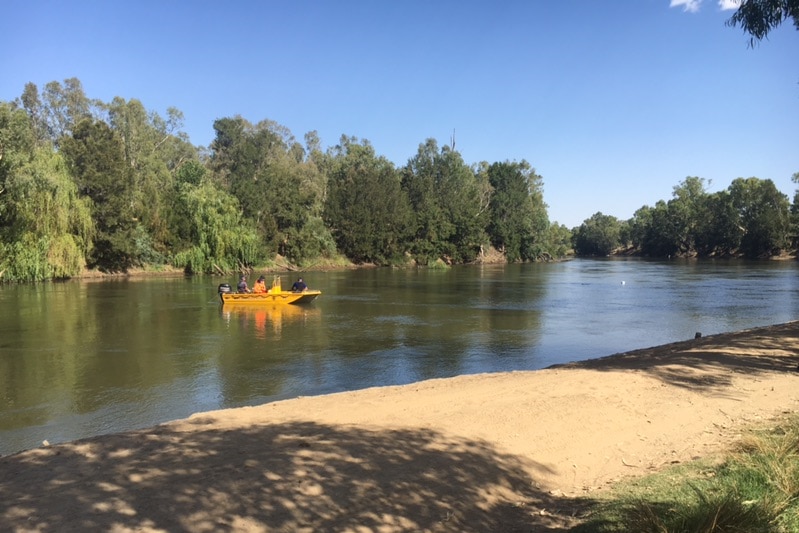 Yellow boat with three men sits in a river beneath clear blue skies.