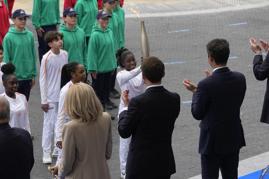 A group of young kids presenting a large torch to men in suits