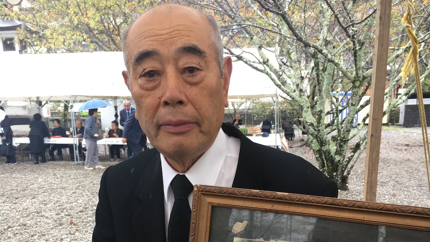 Japanese man wearing suit holds old framed photo of father in uniform