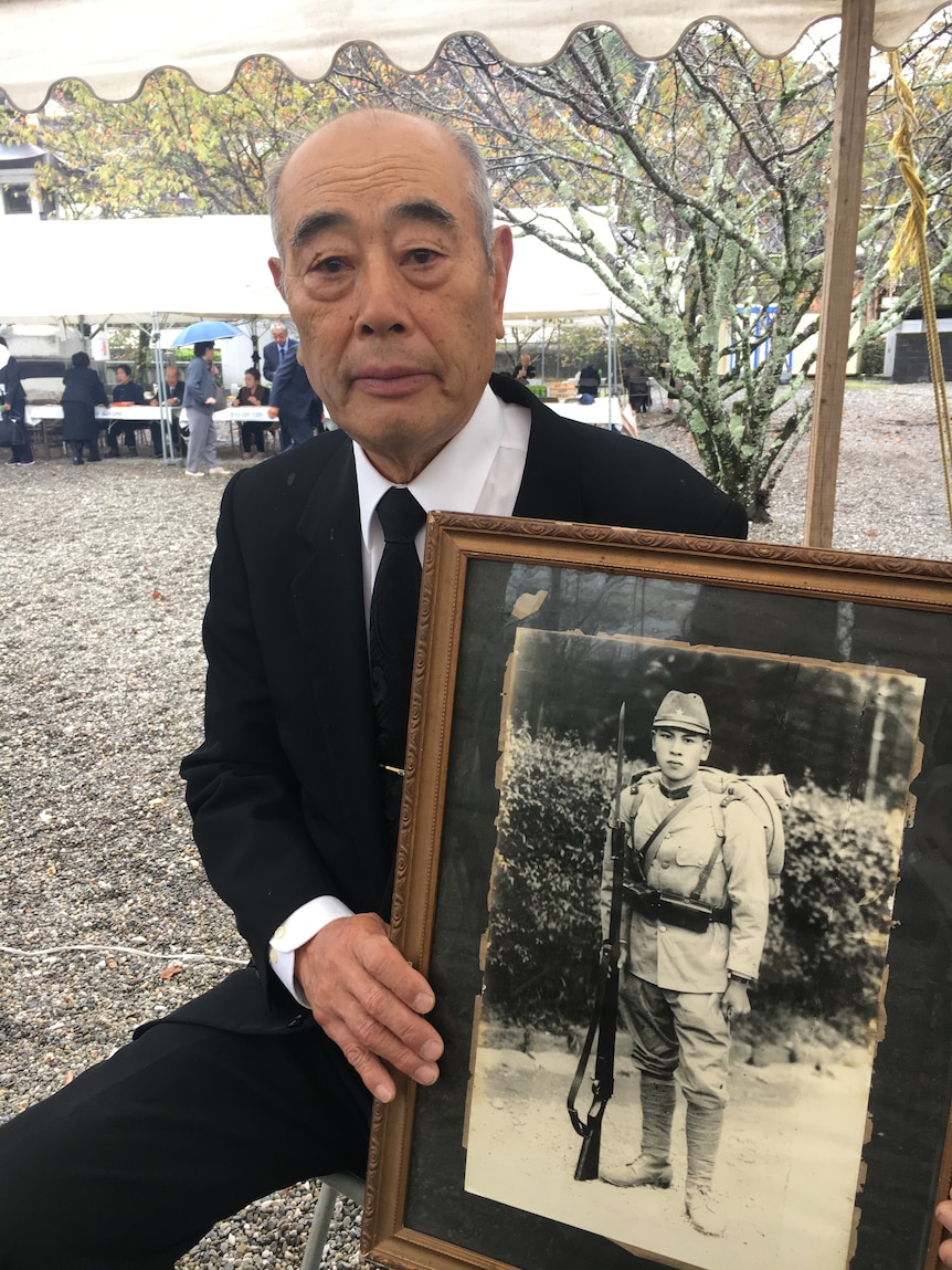 Japanese man wearing suit holds old framed photo of father in uniform