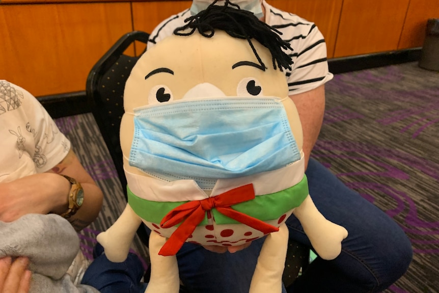 Humpty Dumpty doll sitting on a woman's lap with a face mask on