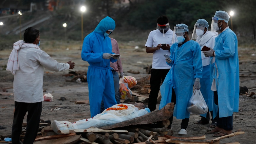 People wearing PPE stand around a deceased relative