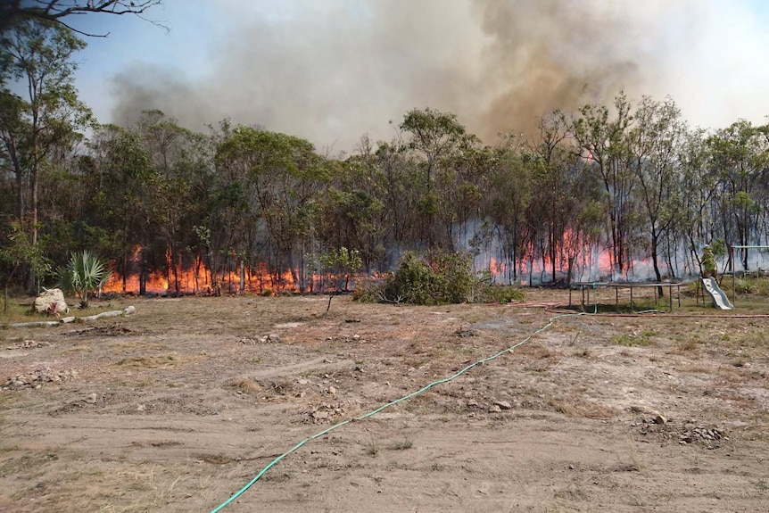 A fire burning in trees with a trampoline, slide and swing set just metres away.