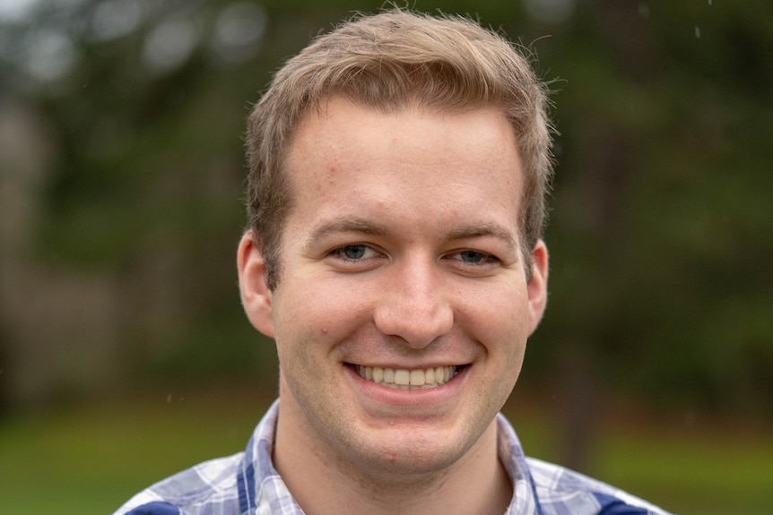 A Caucasian male, wearing a checked shirt, smiling at the camera.