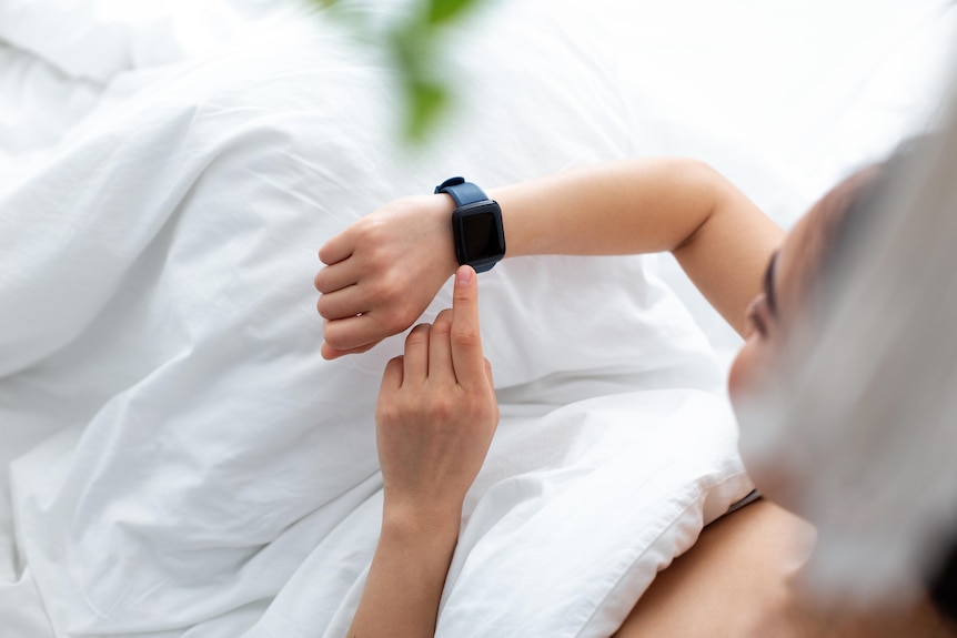Overhead view of a woman in bed looking at her smart watch