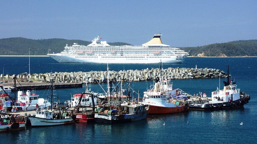 A fishing fleet moored at a wharf with a large cruise ship in the background at Eden on NSW South Coast.