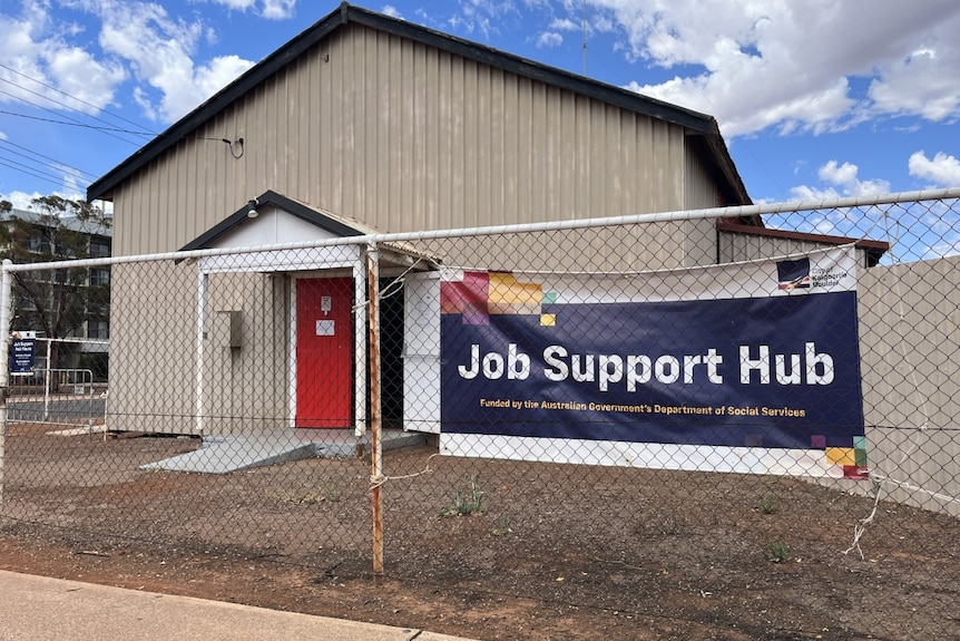A picture of an old hall with a job support sign on a fence 