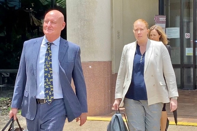 A bald man in a suit walks away from a courthouse ahead of a ginger-haired woman in a light coloured blazer.