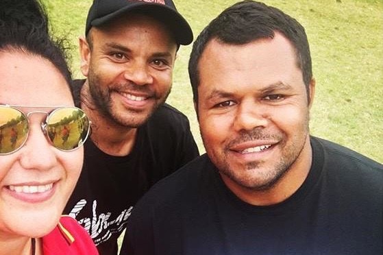 A woman smiles with two men beside her