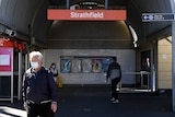 people walk under a sign outside a train station