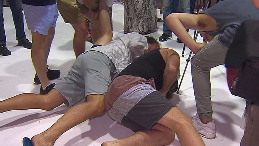 Three men restrain the teenager on the floor.