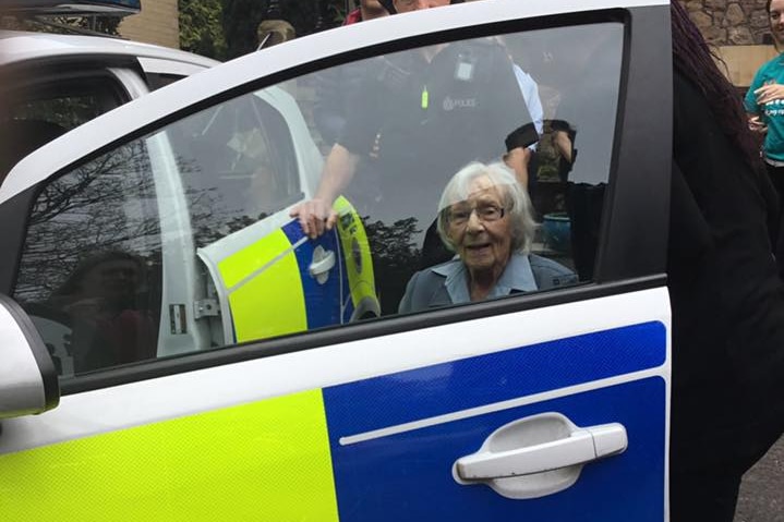 Anne Brokenbrow smiles as she's ushered into a police car.