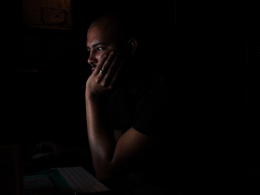 A man looks at a computer screen in the dark.