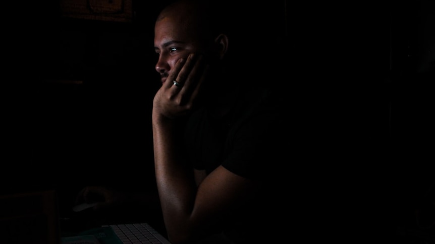 A man looks at a computer screen in the dark.