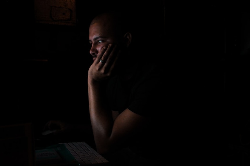 A man looks at a computer screen in the dark.